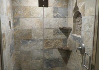A shower room with earthy custom tile walls, an inlet shelf, and corner seat.